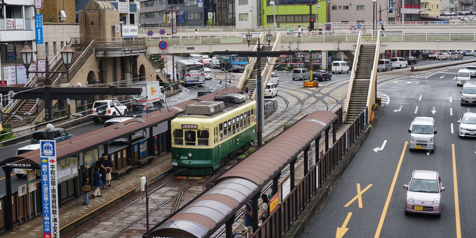 A Nagasaki Electric Tramway streetcar passing through central Nagasaki beneath a pedestrian overpass