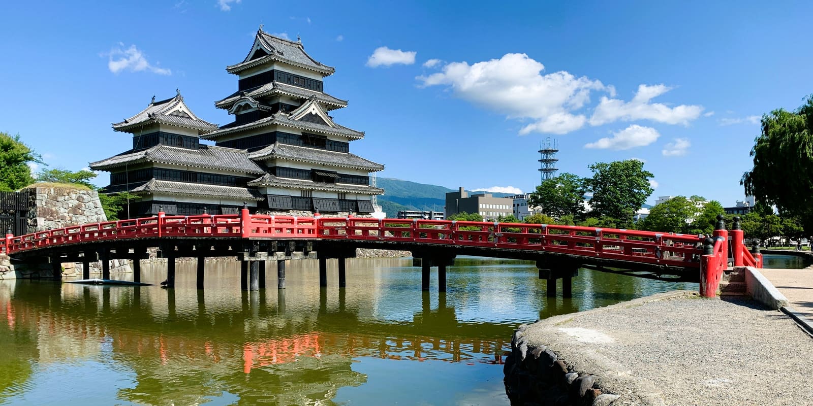 Matsumoto Castle's black-and-white five-story keep reflected in its moat, with the Northern Japan Alps in the background