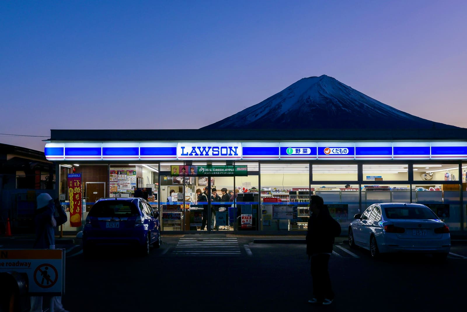 A Lawson convenience store lit up at dusk with Mount Fuji visible behind it, illustrating the everyday konbini experience in Japan