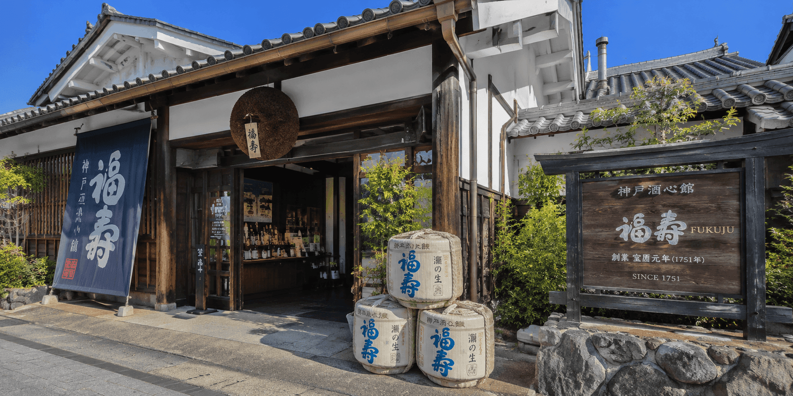 Traditional wooden entrance and sake barrels at Kobe Shushinkan, the Fukuju sake brewery, with a sign reading Kobe Shushinkan Fukuju since 1751