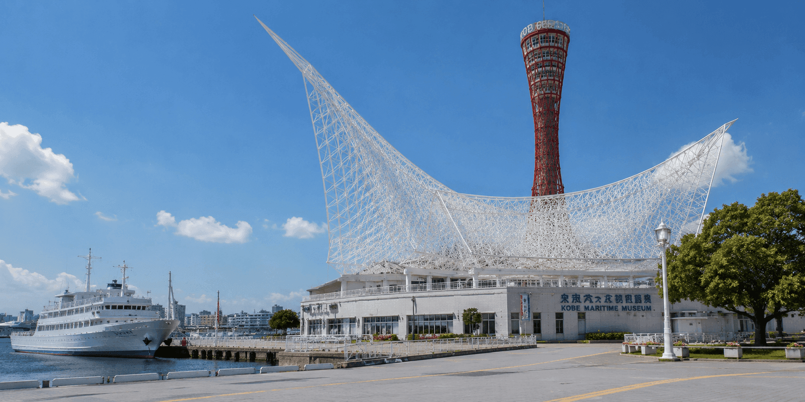 White lattice sail-shaped roof of Kobe Maritime Museum beside the red Kobe Port Tower with a docked ship in Meriken Park
