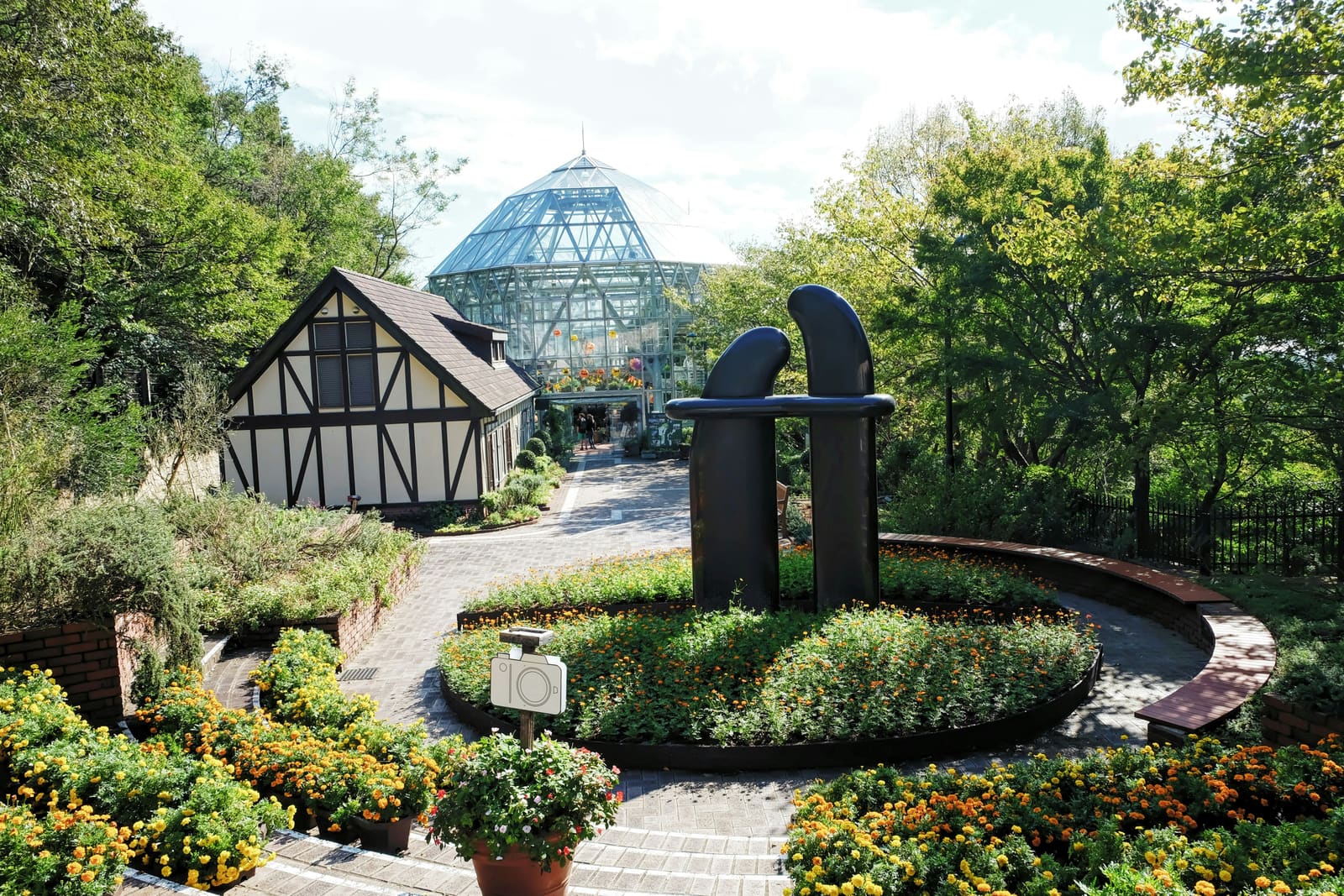 The glass greenhouse dome and marigold garden beds at Kobe Nunobiki Herb Gardens, with a Tudor-style building nearby