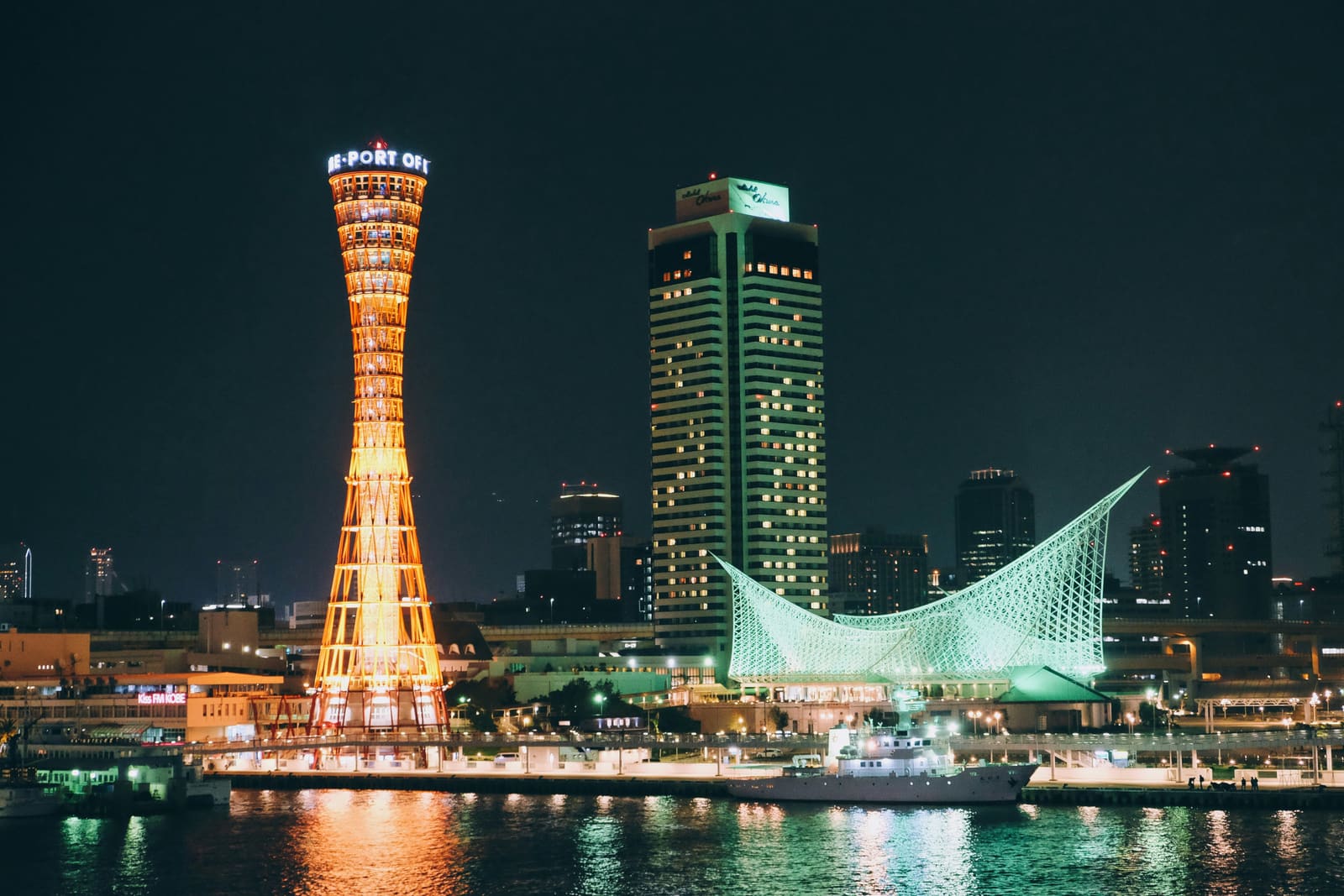 Kobe Port Tower illuminated at night beside the sail-shaped Kobe Maritime Museum on the Meriken Park waterfront