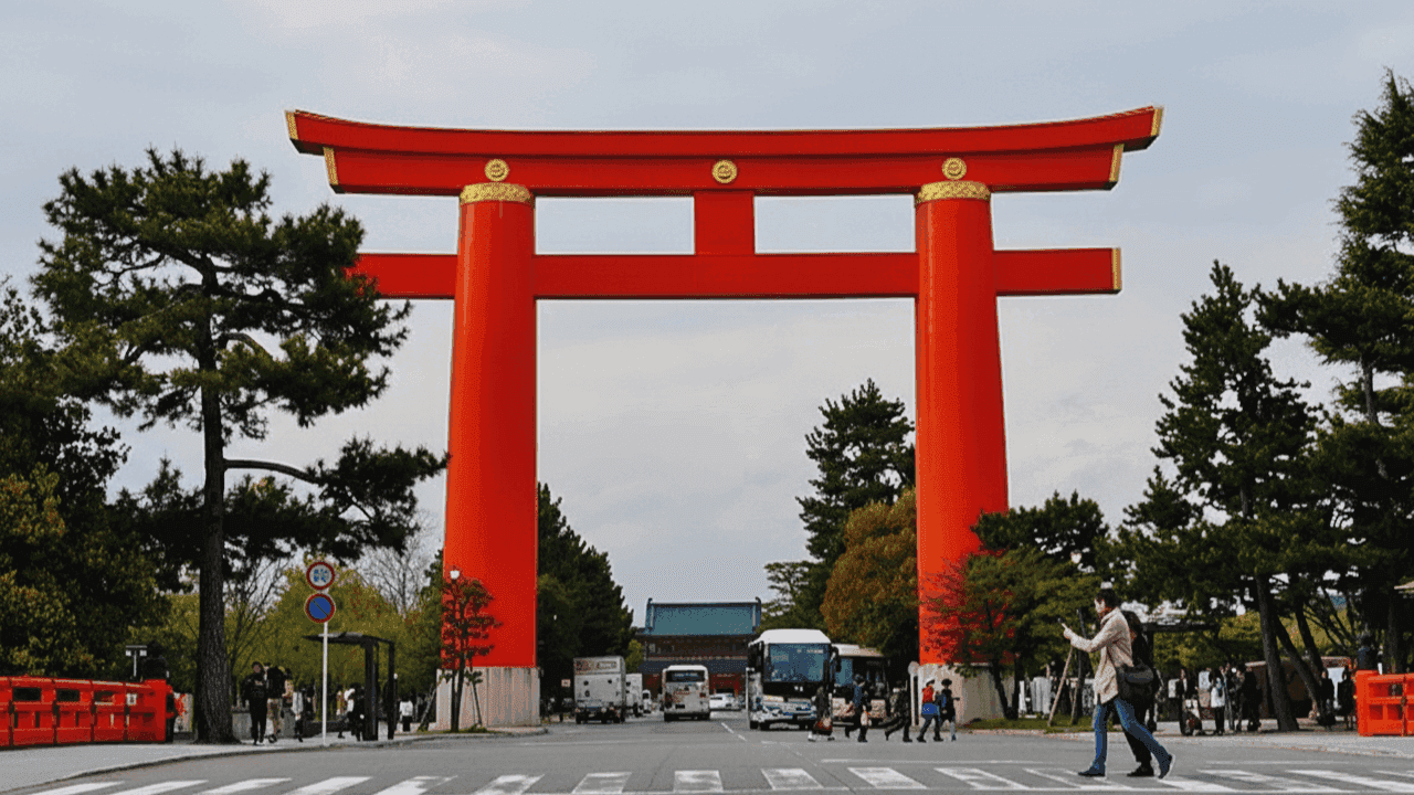 The great vermilion torii of Heian Shrine over the approach road in Okazaki, with the Otenmon gate in the distance and a pedestrian crossing in front