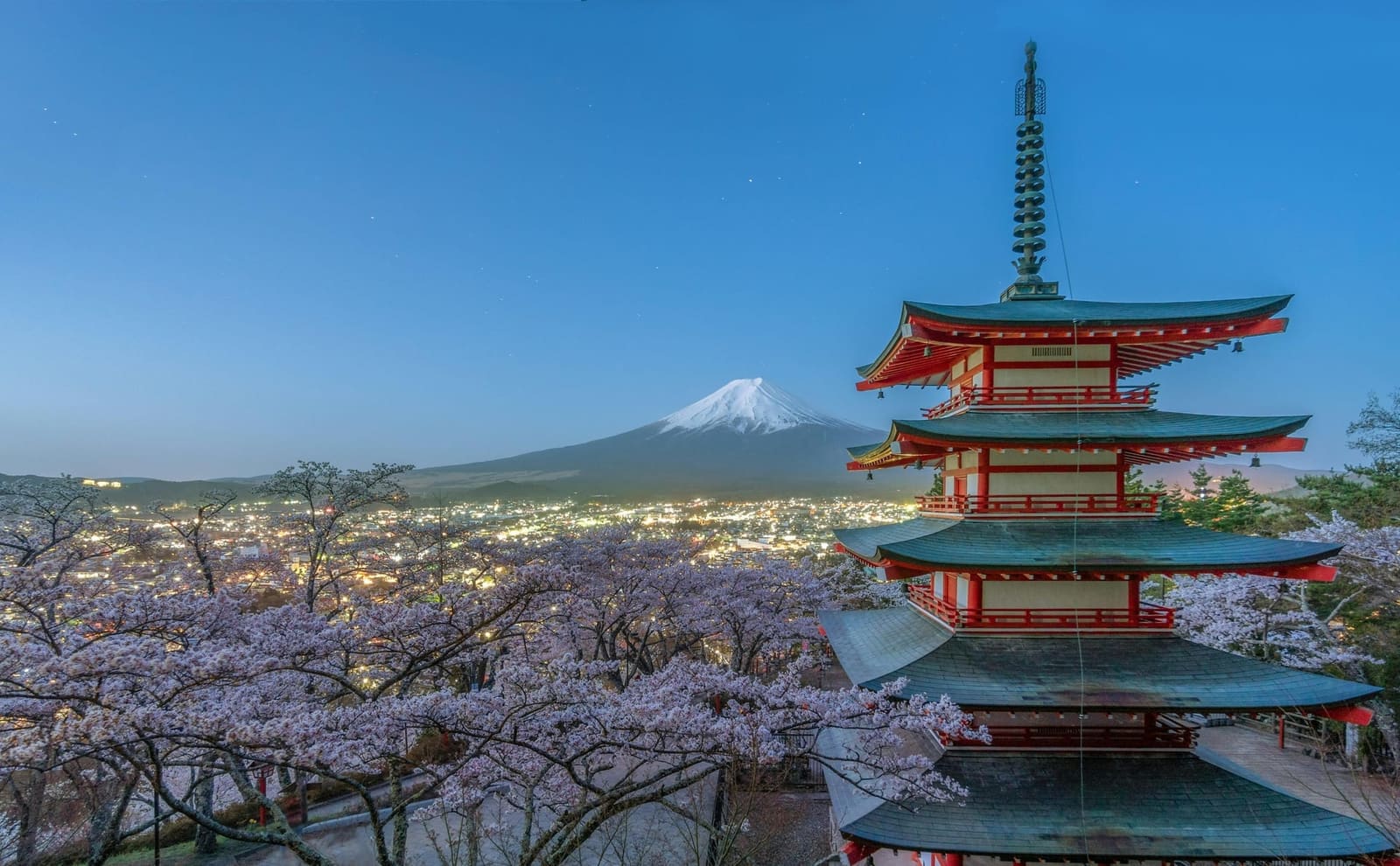 Chureito Pagoda with cherry blossoms in bloom and Mount Fuji behind the lights of Fujiyoshida at dusk