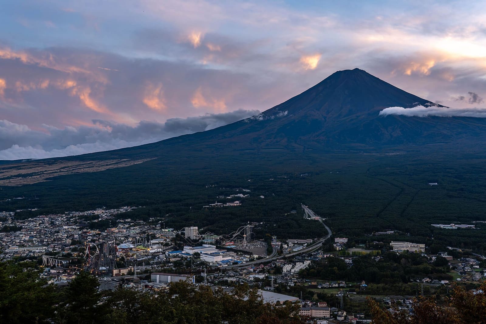 Fuji-Q Highland and the town of Fujiyoshida below Mount Fuji at dusk, with roller coaster tracks at the lower left