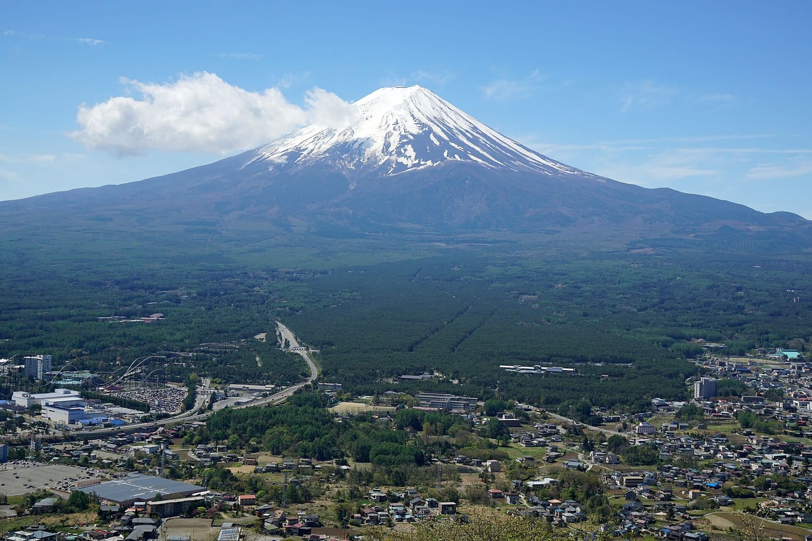 Snow-capped Mount Fuji above forest and the town of Fujiyoshida, seen from the top of Mount Tenjo in spring