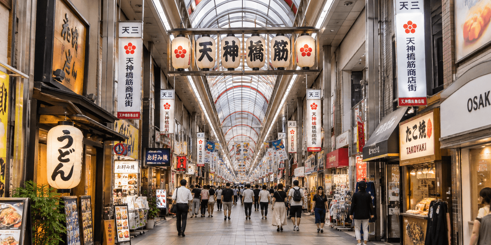 Covered Tenjinbashisuji Shopping Street arcade with a row of hanging paper lanterns, banner signs, udon and takoyaki shopfronts, and shoppers walking toward the far end, Osaka, Japan