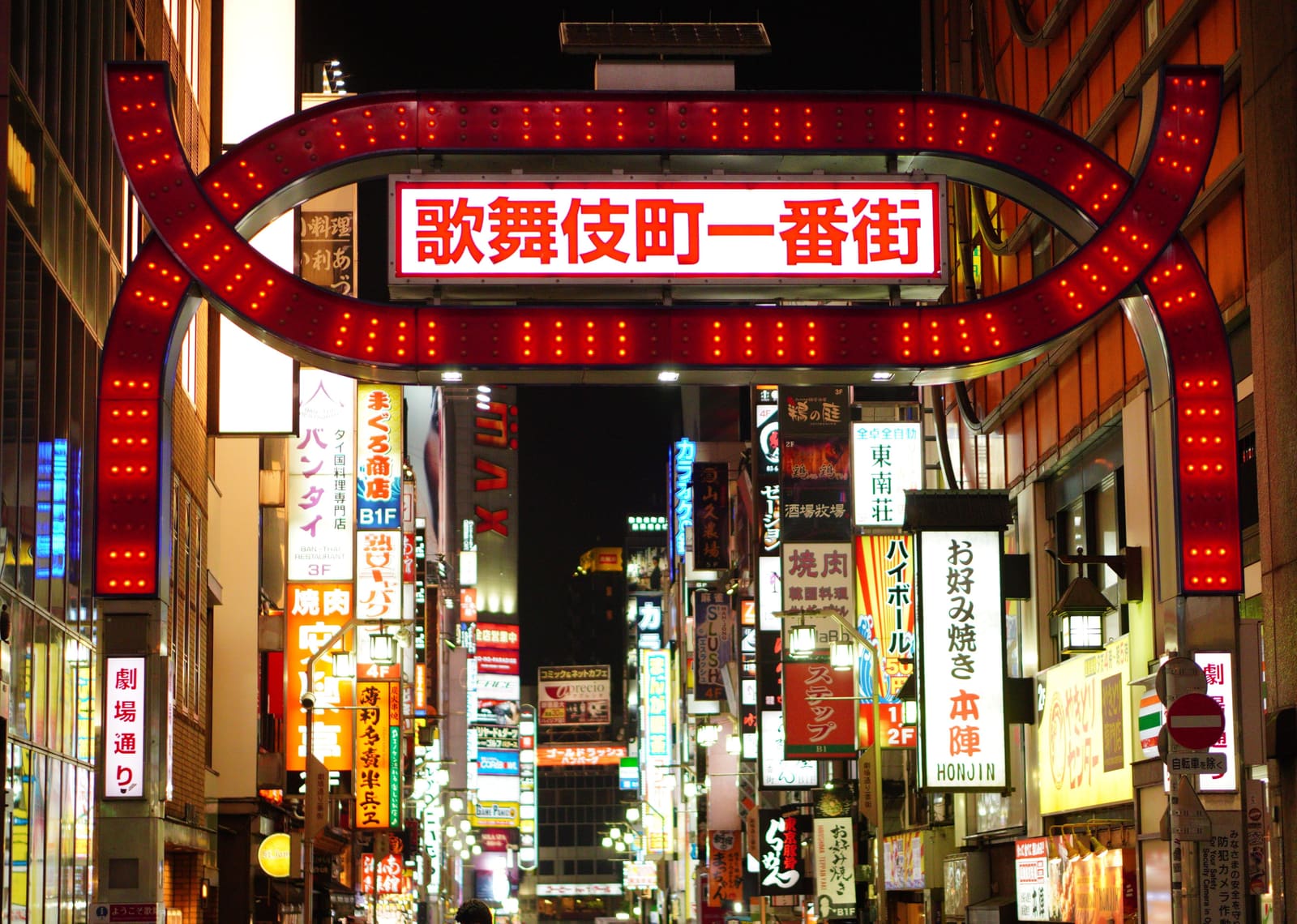 Kabukicho entertainment district entrance arch glowing with red neon lights and Japanese signs at night in Shinjuku, Tokyo