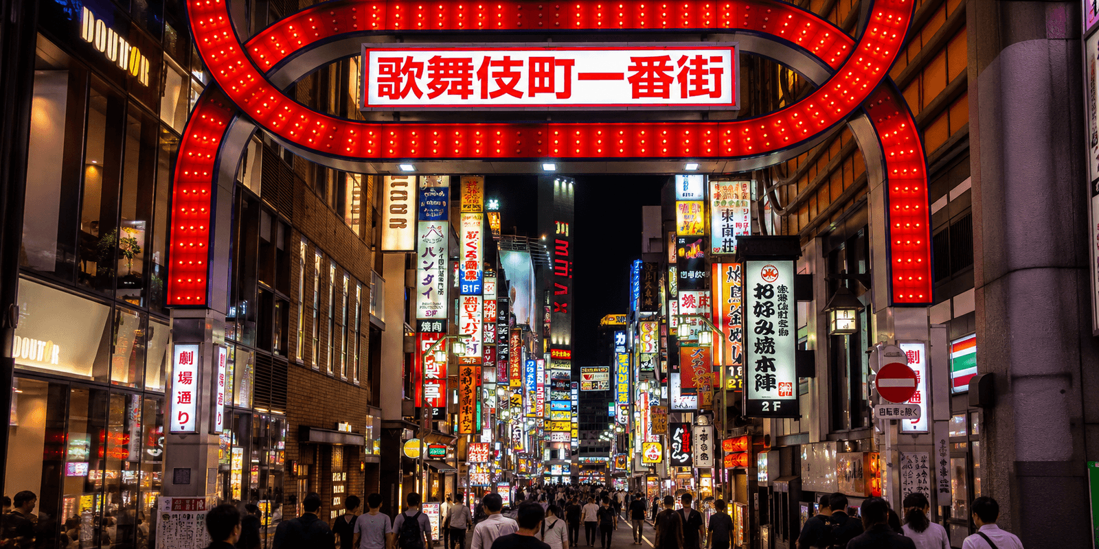 The illuminated red Kabukicho Ichiban-gai gate at night, with dense neon signs and crowds filling the street beyond, Shinjuku, Tokyo, Japan