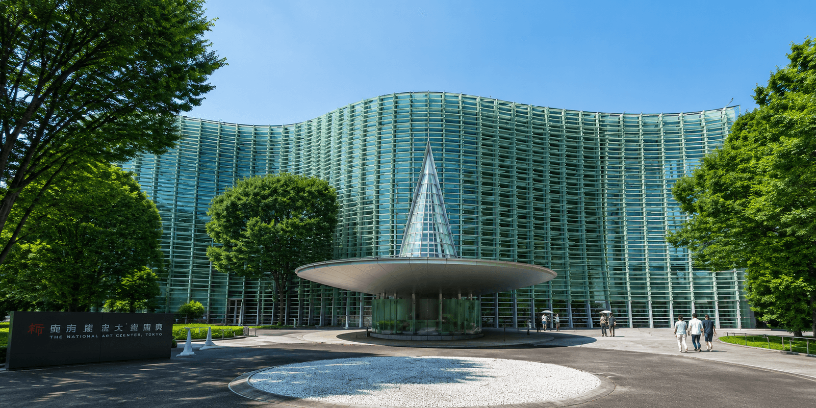 The National Art Center, Tokyo's undulating glass facade and inverted cone entrance structure, with mature trees framing the plaza