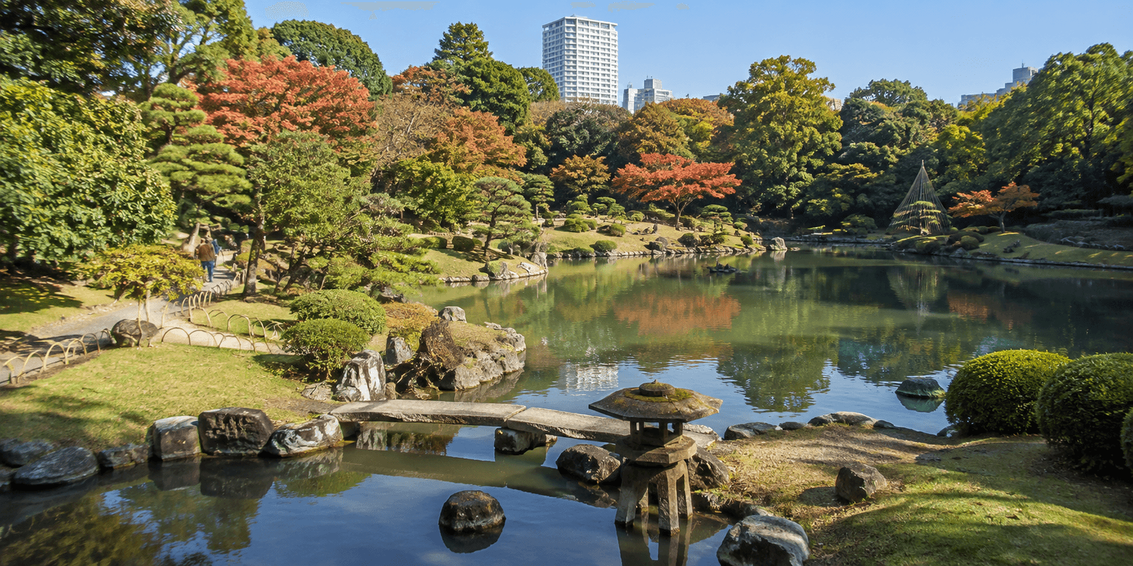 Rikugien Gardens' central pond and autumn maple foliage with the Tokyo skyline behind it, Bunkyo, Tokyo, Japan