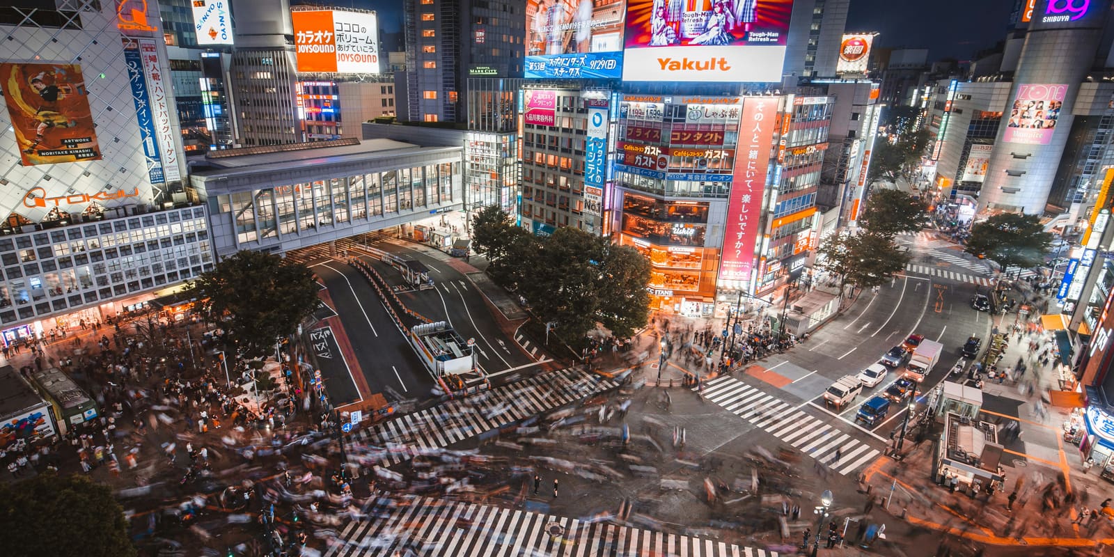 Crowds crossing the Shibuya Scramble Crossing at night beneath illuminated billboards