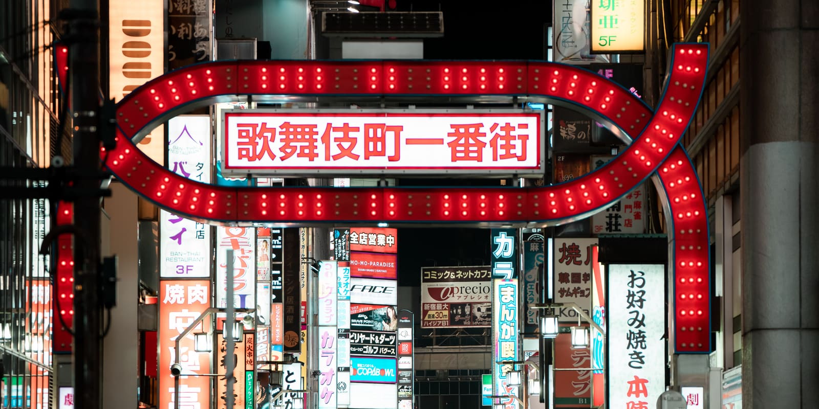 The red lit gate of Kabukicho Ichibangai in Shinjuku at night, with neon signs for karaoke and restaurants beyond