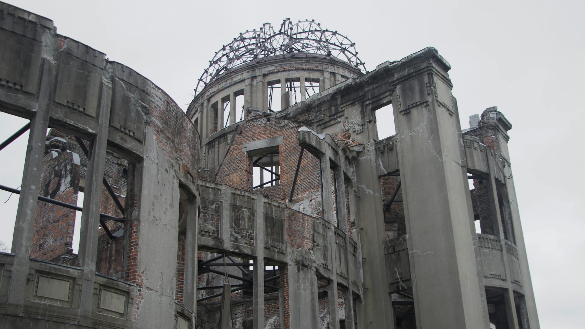 Atomic Bomb Dome preserved ruins with skeletal iron dome frame and brick walls against grey sky, Hiroshima Japan