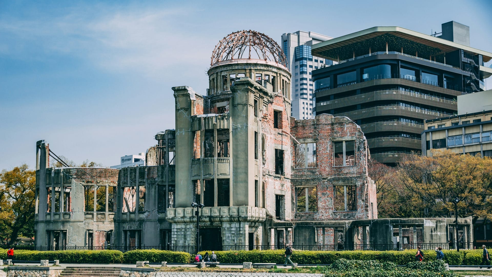 Atomic Bomb Dome wide view with preserved ruins surrounded by Peace Memorial Park gardens under blue sky, Hiroshima Japan