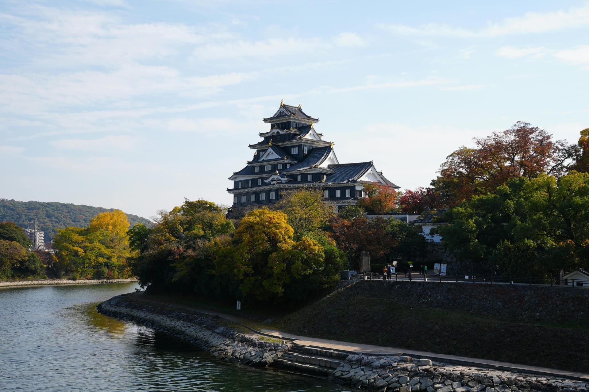 Hiroshima Castle five-storey keep viewed from across the moat with autumn trees and blue sky, Japan