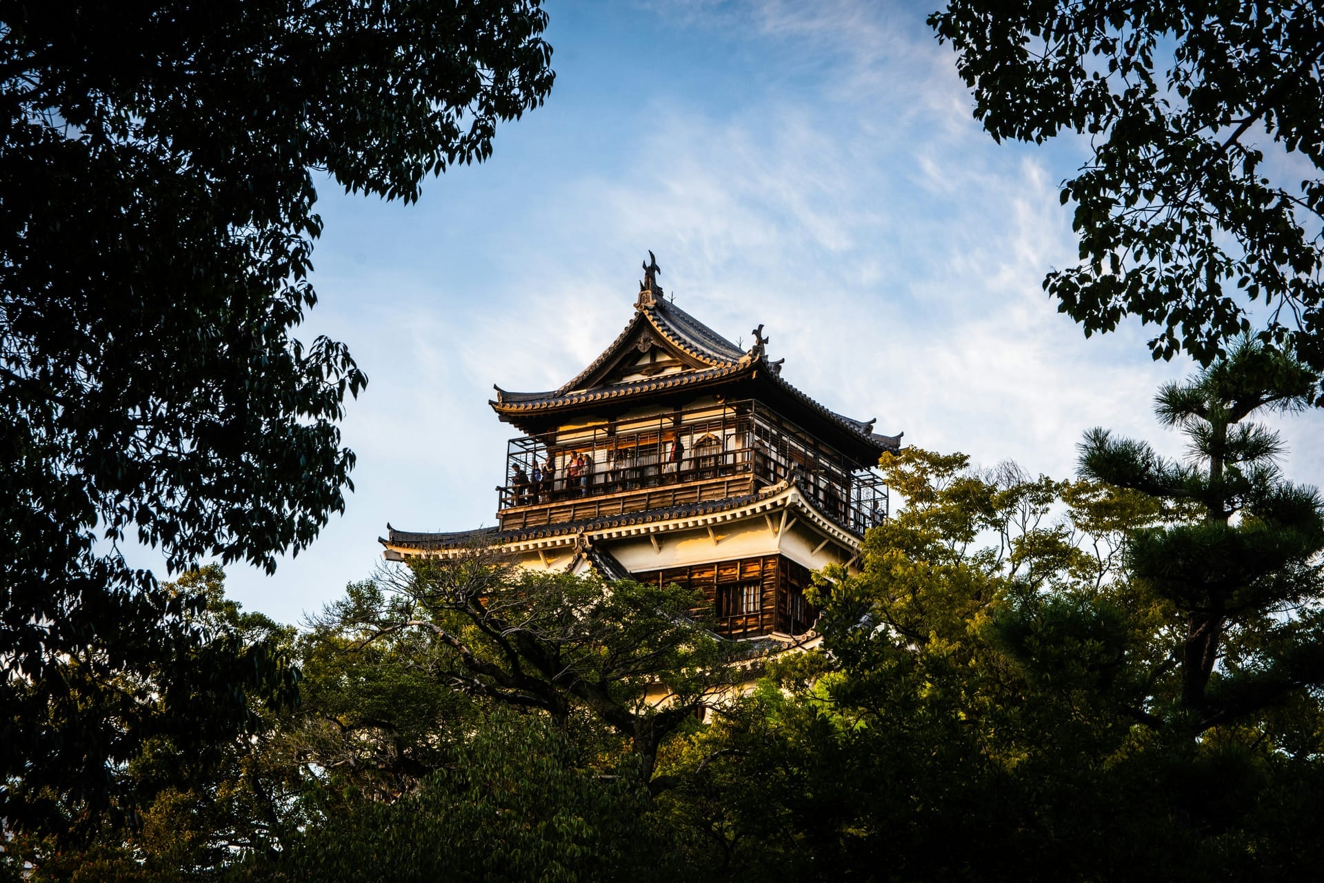 Hiroshima Castle keep framed by green trees with warm evening light and blue sky, Japan