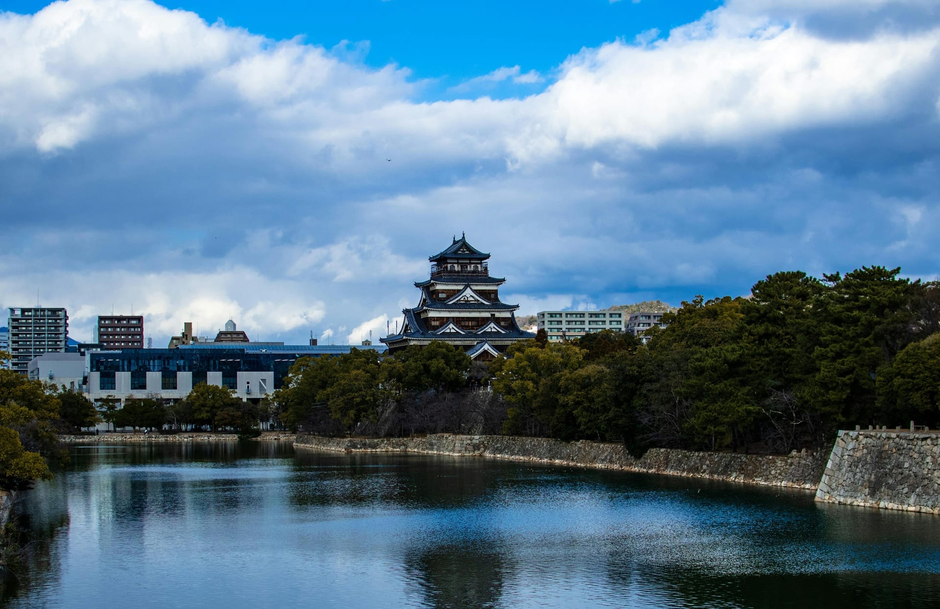 Hiroshima Castle and stone-walled moat under dramatic clouds with the surrounding city in the distance, Japan
