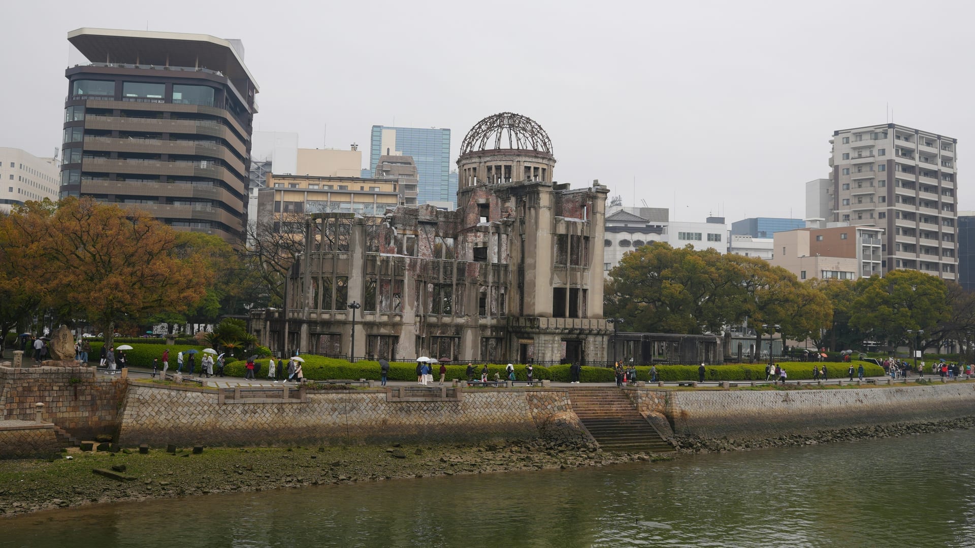 A-Bomb Dome viewed from across the Motoyasu River with visitors walking along the riverbank, Hiroshima Japan