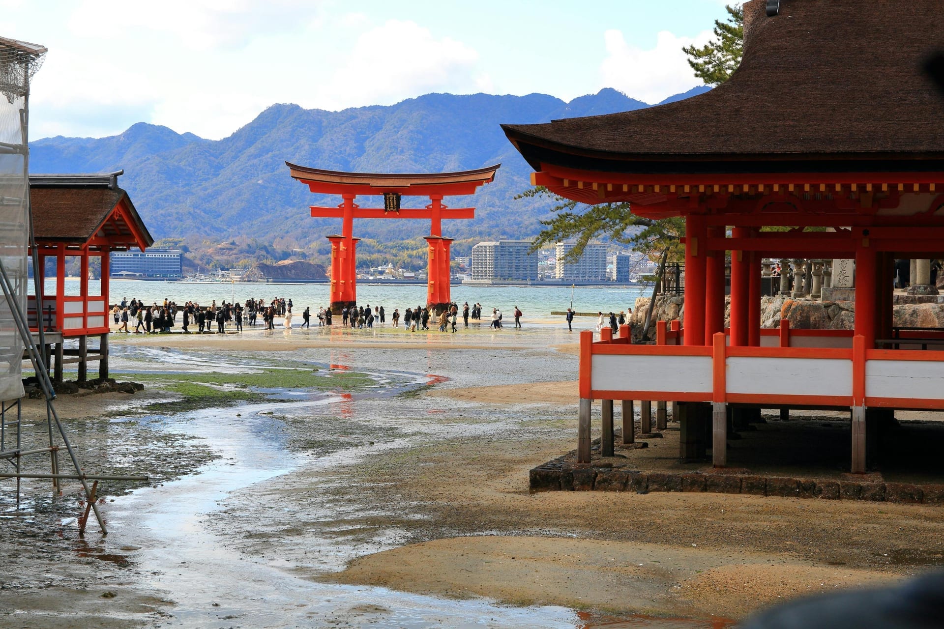 Itsukushima Shrine torii gate and traditional shrine buildings at low tide with mountains behind, Miyajima Island Japan