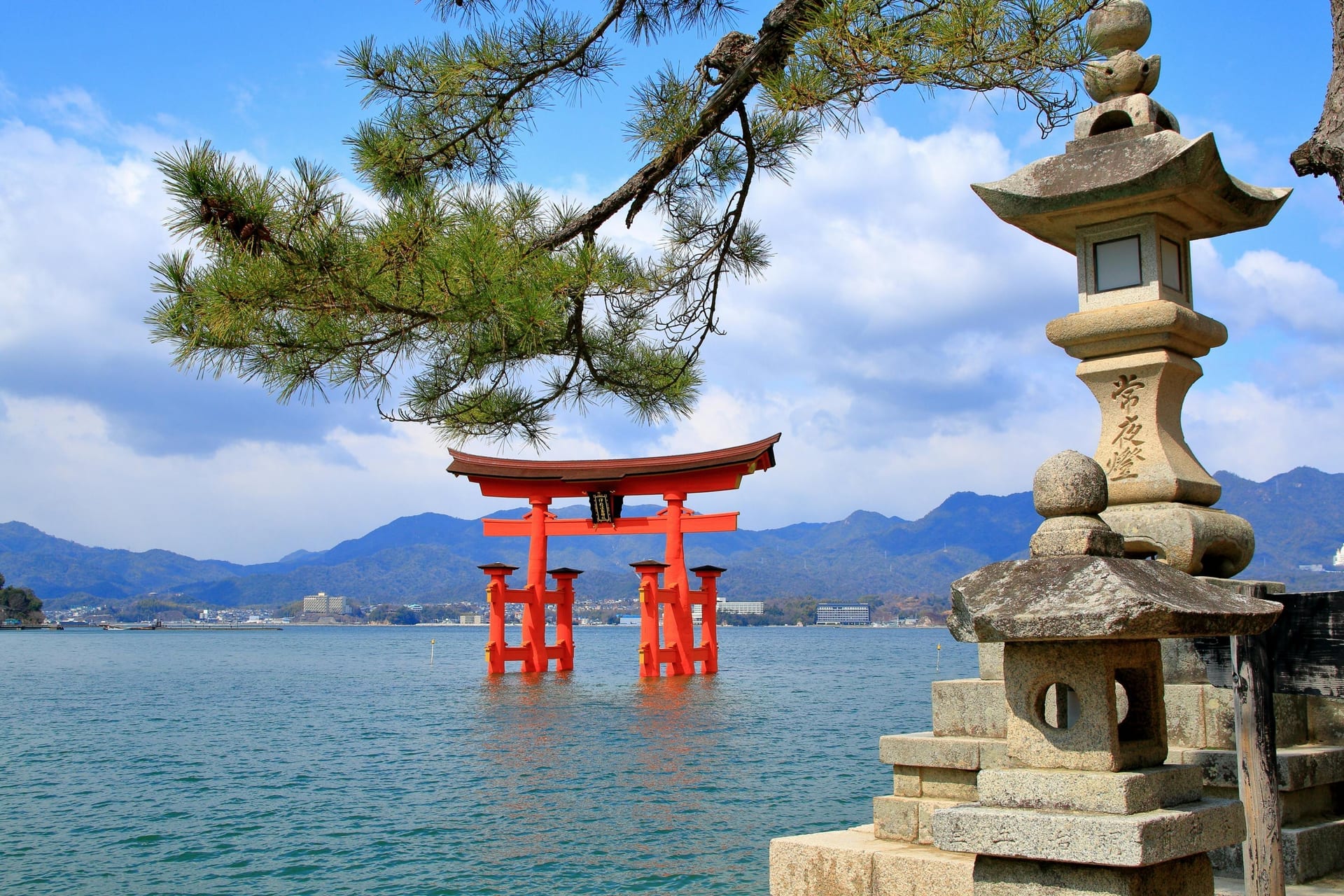 Itsukushima torii gate framed by pine tree branches with stone lantern and blue sky, Miyajima Island Japan
