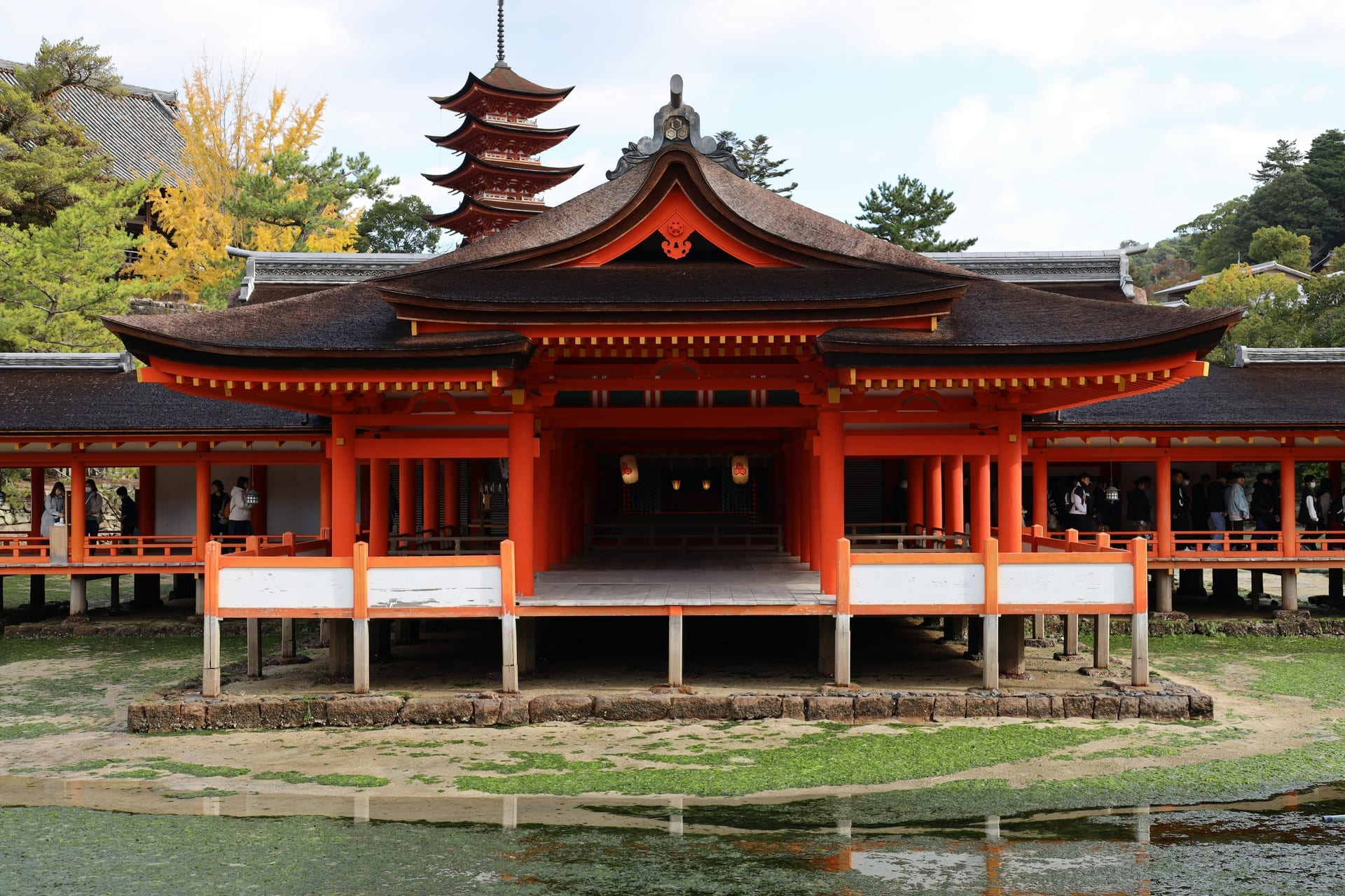 Itsukushima Shrine main hall on stilts with five-storey pagoda visible through the trees, Miyajima Island Japan