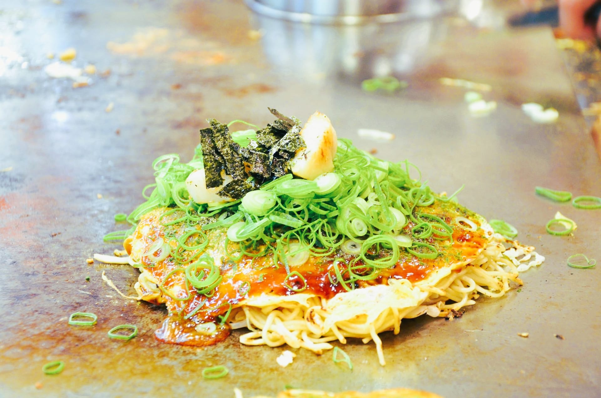 Hiroshima-style okonomiyaki on a teppan grill topped with green onions, nori, and sauce, Japan