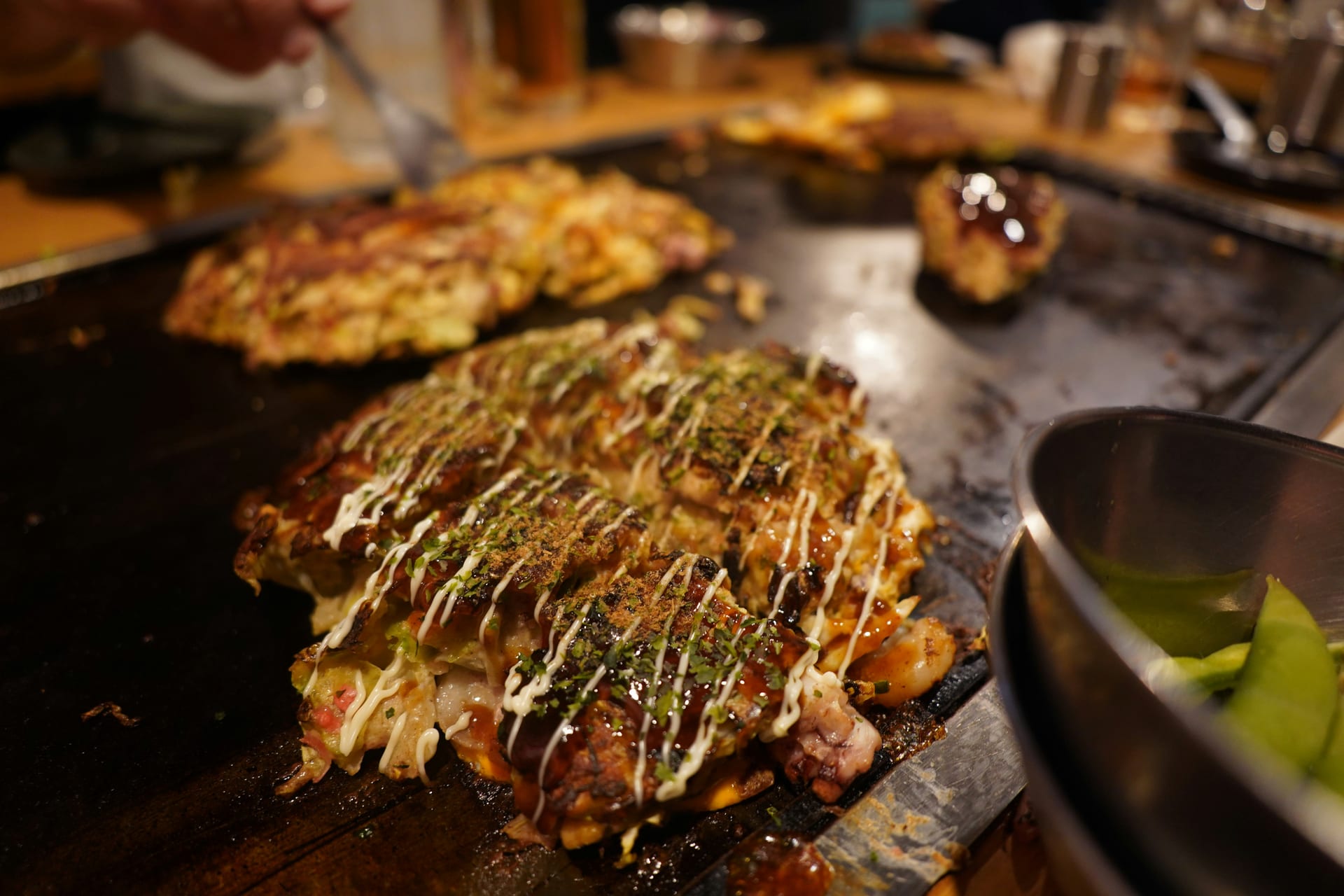 Hiroshima okonomiyaki cooking on a teppan grill with aonori and mayonnaise, Japan
