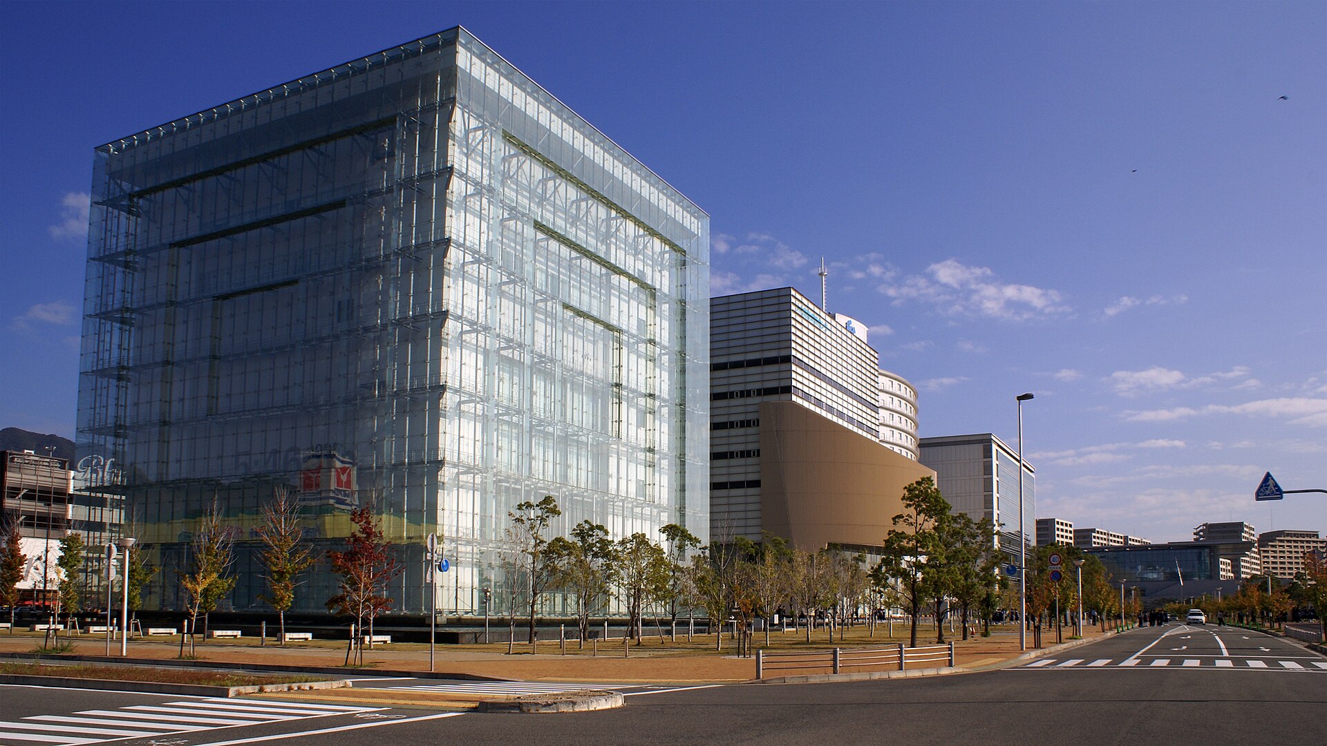 The glass-walled exterior of the Disaster Reduction and Human Renovation Institution at HAT Kobe, with the Rokko mountain range in the distance