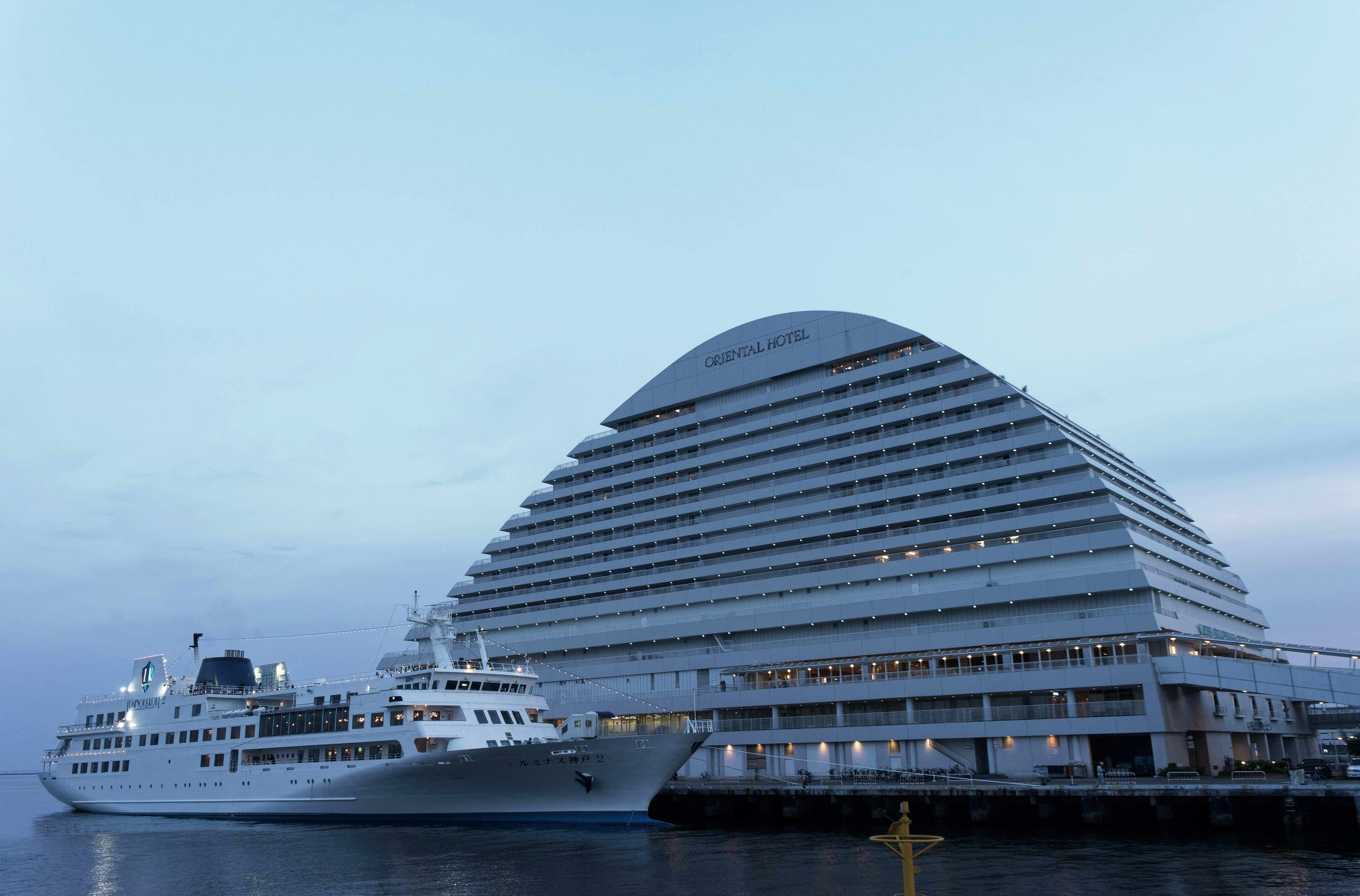 The Kobe Meriken Park Oriental Hotel and a docked sightseeing ship on the Meriken Park waterfront at dusk