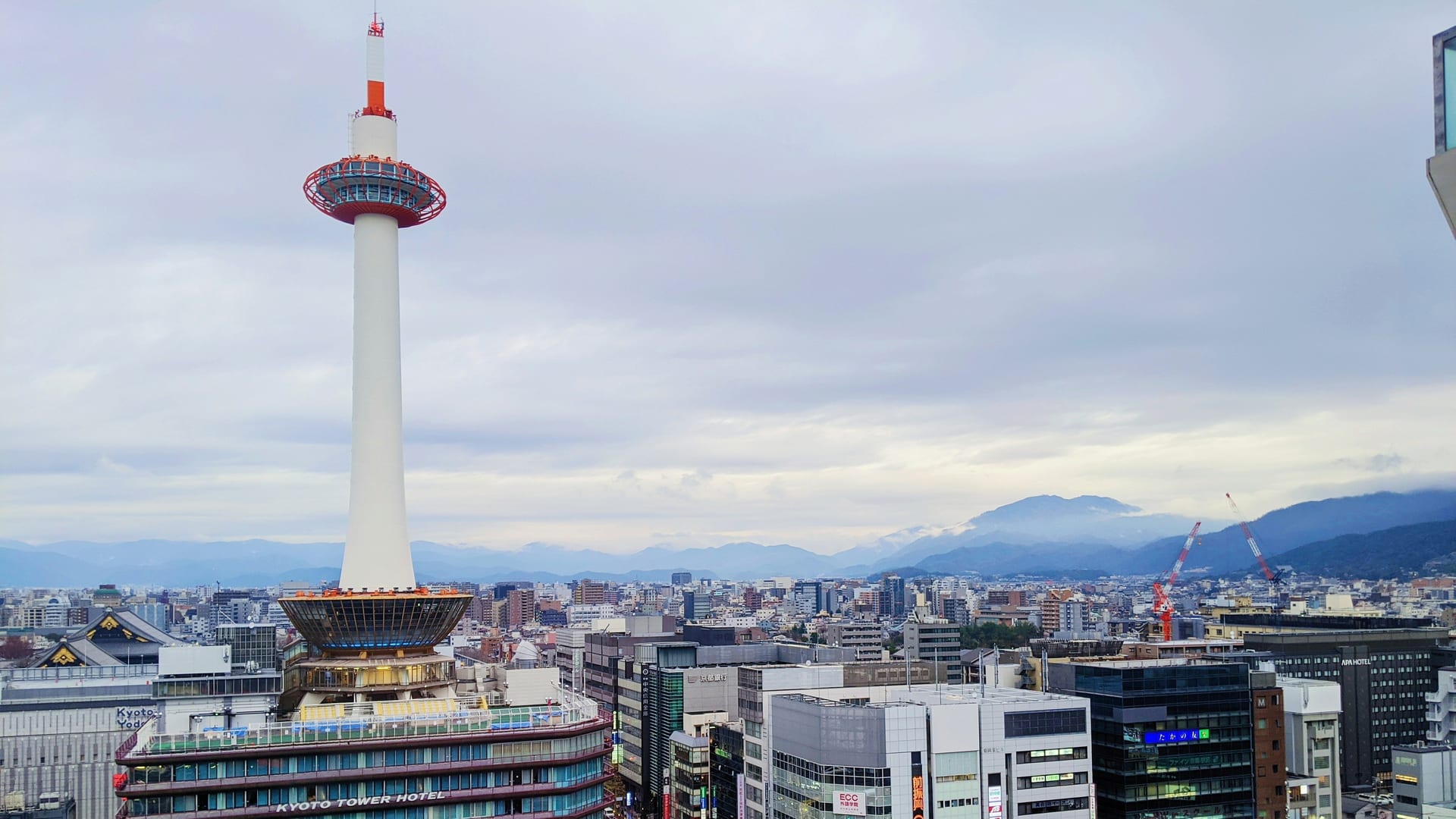 Kyoto Tower rising above Kyoto Station with the city skyline and surrounding mountains visible in the background