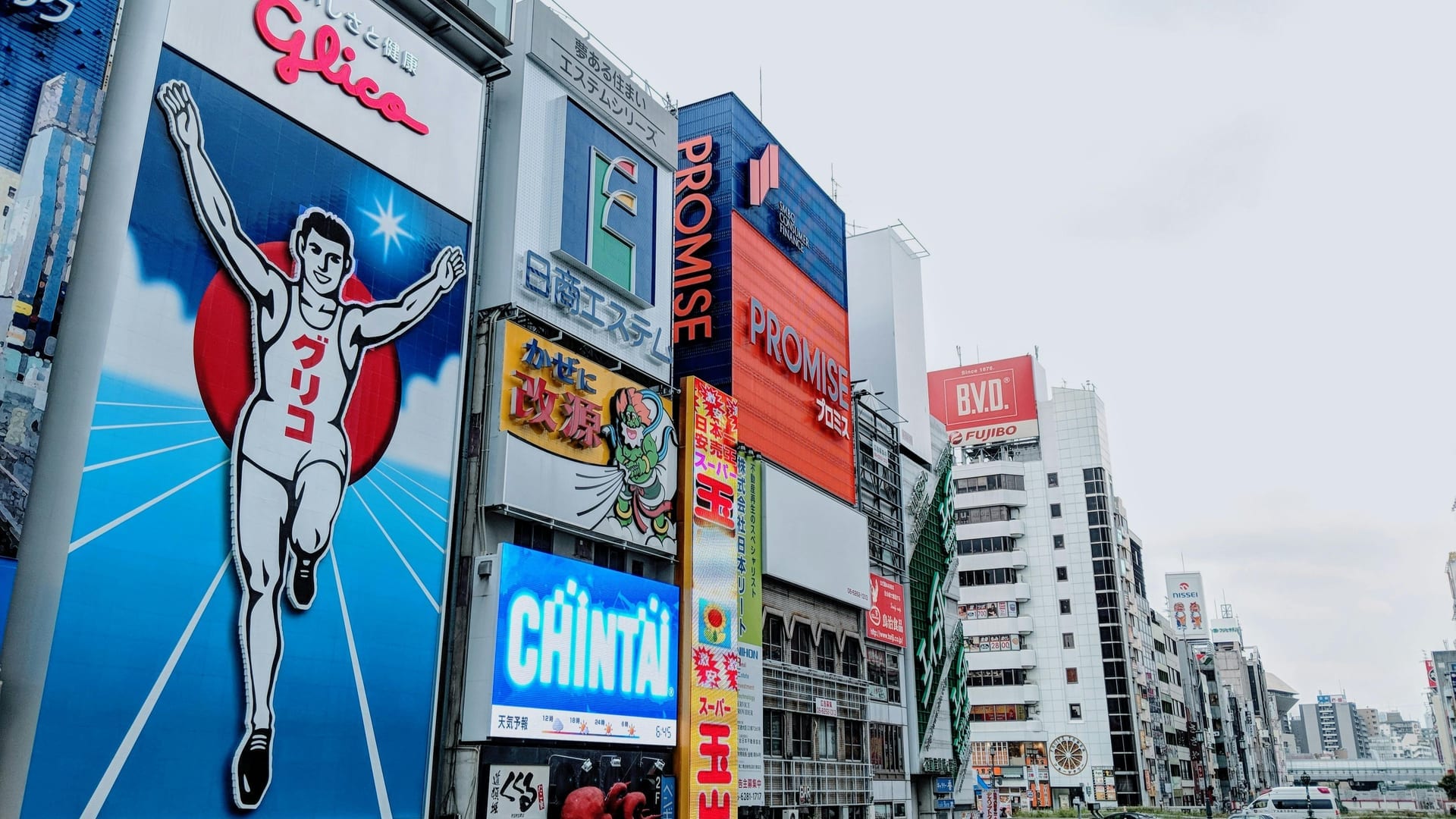 Dotonbori canal at night with giant neon signs and the iconic Glico Running Man billboard reflected in the water, Osaka